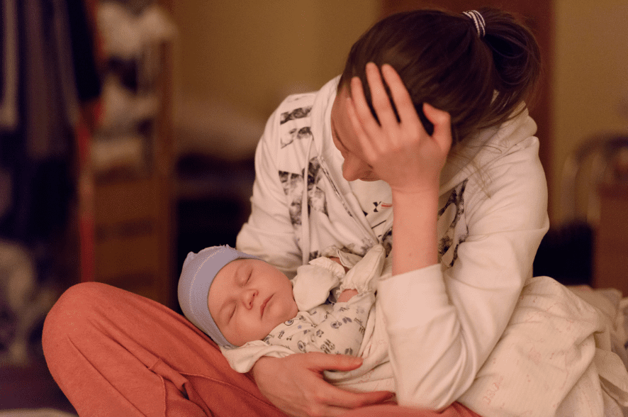 A mother holding her baby while appearing distressed.