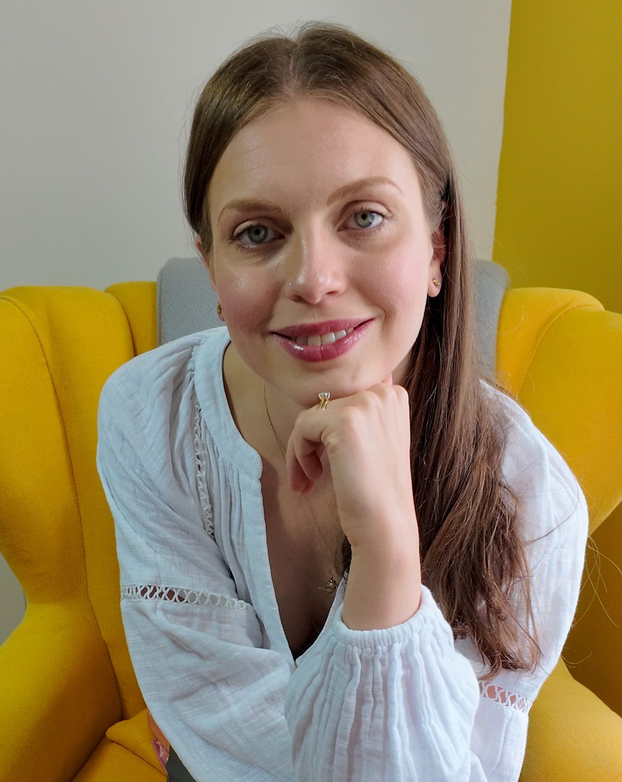 Megan Baldry, perinatal Counsellor and Psychotherapist, headshot taken whilst wearing a white top and sat on a yellow armchair