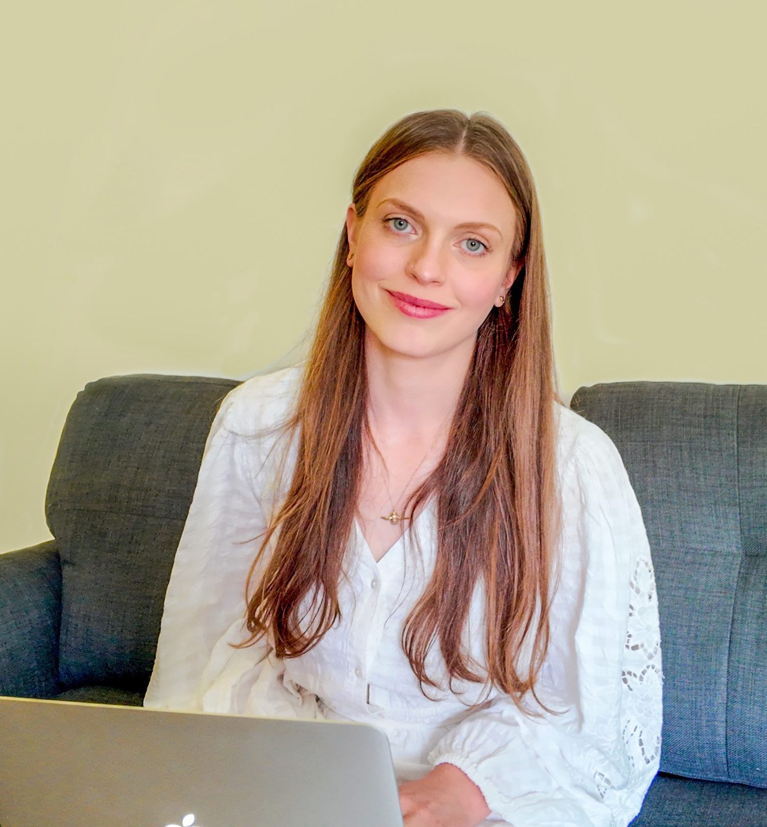 Megan Baldry, Perinatal Counsellor and Psychotherapist, sat on a sofa with a laptop and wearing a white dress