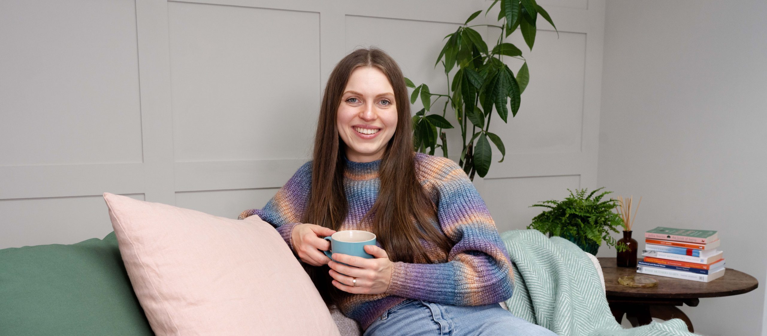 Megan sat on the sofa with a mug of tea and surrounded by perinatal mental health books